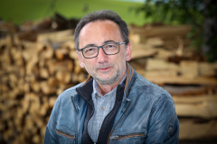 Lutz Scheufler (Nahaufnahme) vor Stapel mit gefällten Baumstämmen