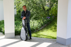 Lutz Scheufler mit Gitarrenkoffer zwischen zwei Pfeilern vor Garten